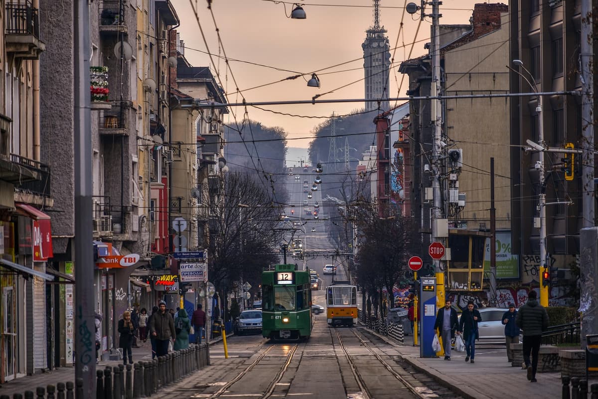 Vasil Levski Boulevard in Sofia with green tram number 12 and yellow tram, apartment buildings with Cyrillic signage and Vitosha mountains in the background