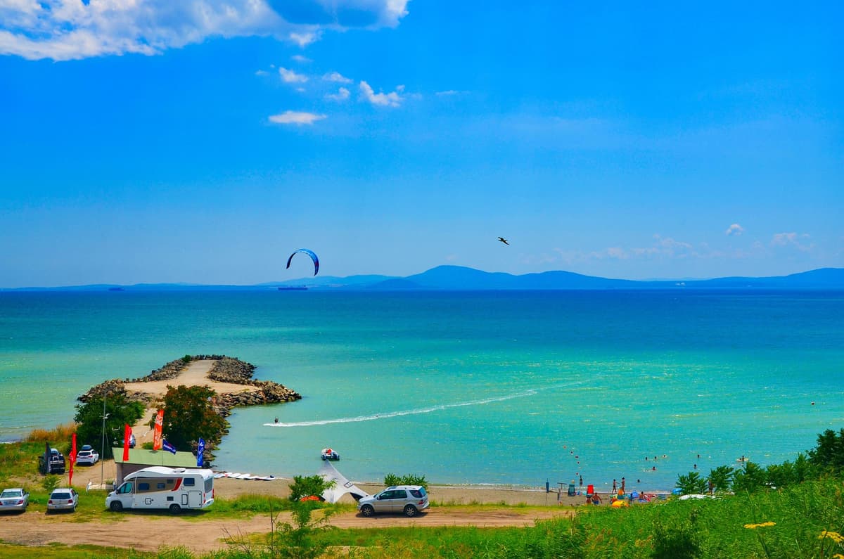 Burgas Bay coastline in Bulgaria with turquoise Black Sea water, stone breakwater and camper van parked against Strandzha mountains backdrop