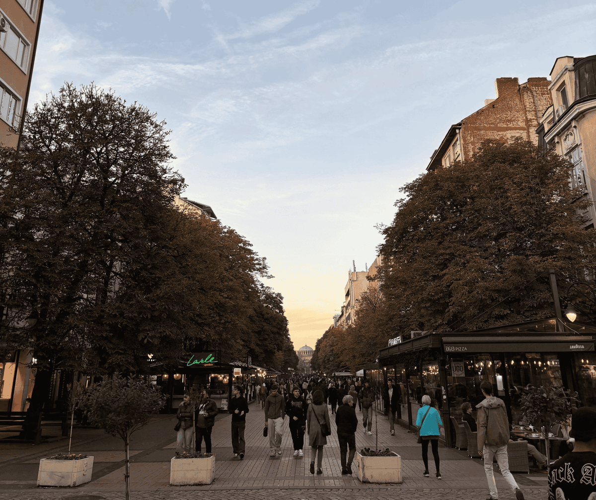 Vitosha Boulevard in Sofia at sunset, pedestrian promenade with restaurants and crowds, autumn chestnut trees, and Sveta Nedelya Cathedral in the distance